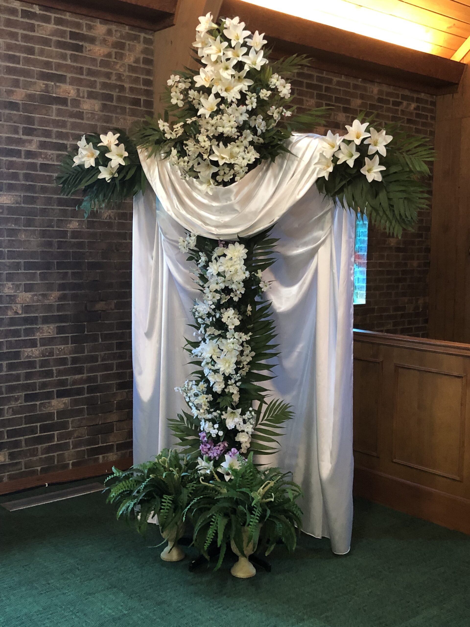A white cross adorned with flowers and greenery, symbolizing faith at a Presbyterian Church.