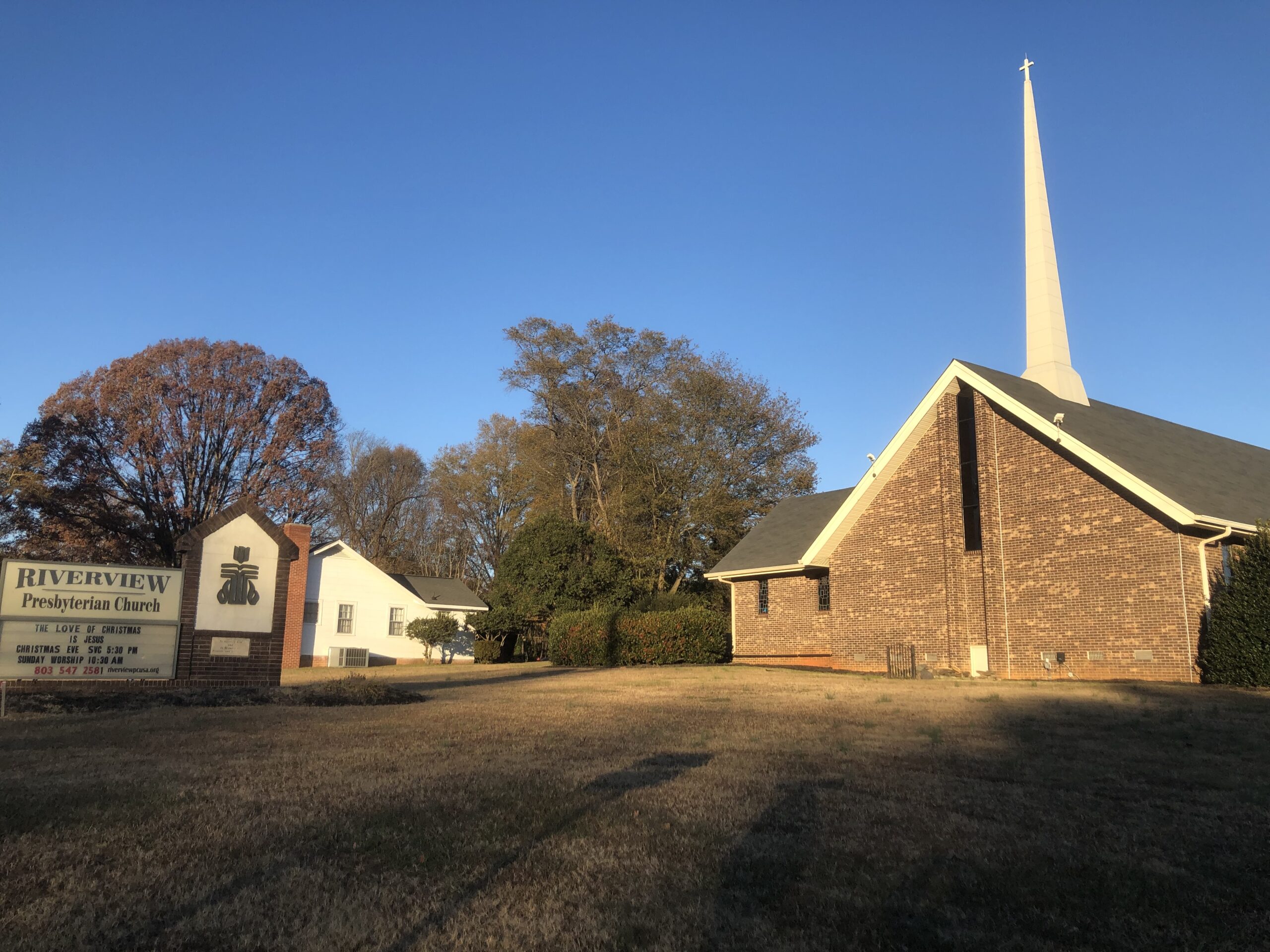A Presbyterian Church with a tall steeple, perched on a scenic hill, surrounded by greenery and blue sky.