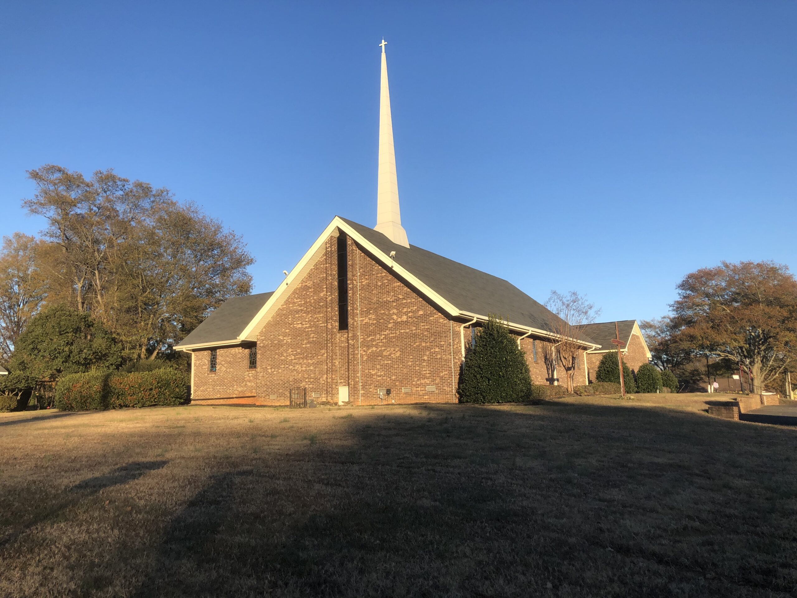 A Presbyterian Church with a tall steeple, perched on a scenic hill, surrounded by greenery and blue sky.